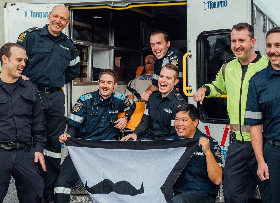 Photo showing first responders holding a Movember-branded flag.
