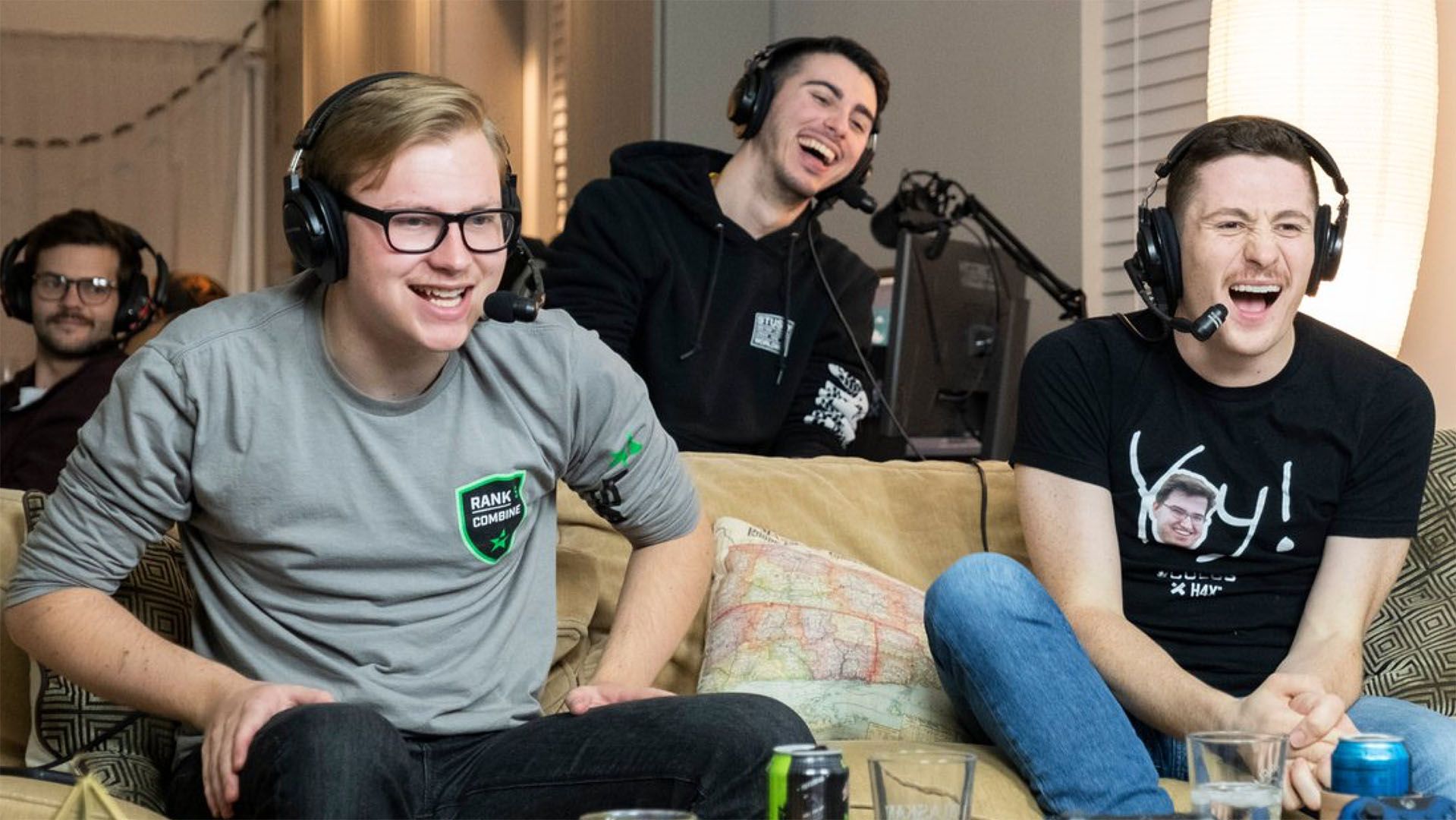 A group of young men laughing while gaming with headsets in. 