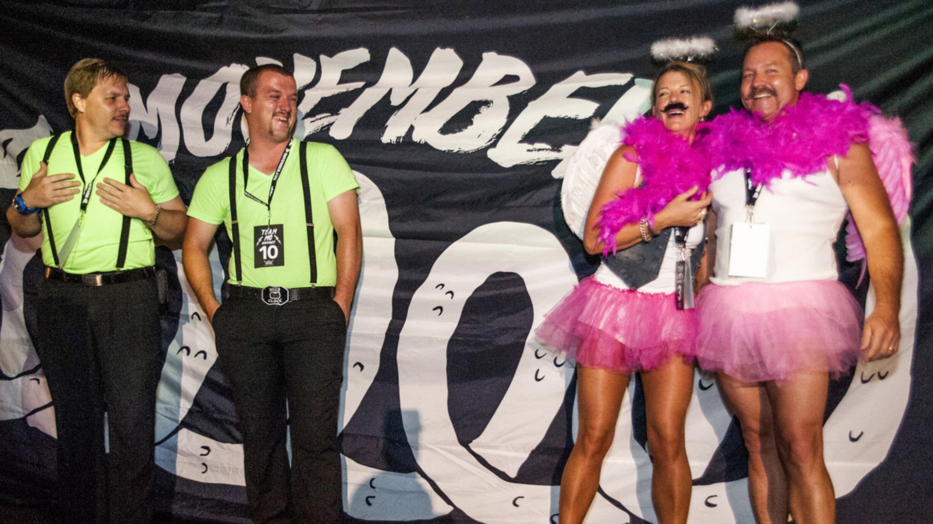 Photo showing four people in humorous fancy dress costume, on a stage and about to win a Movember award.