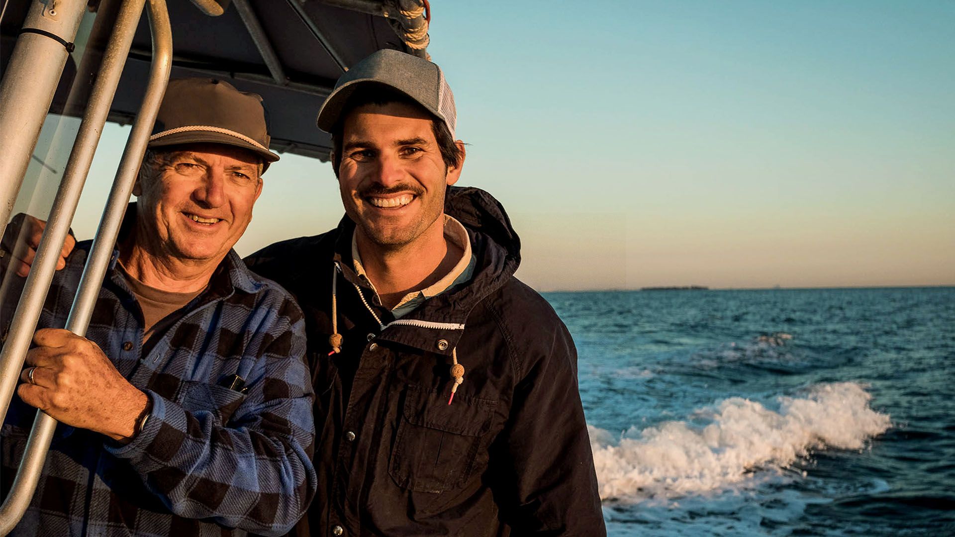 Photo of two men on fishing boat, smiling to camera.